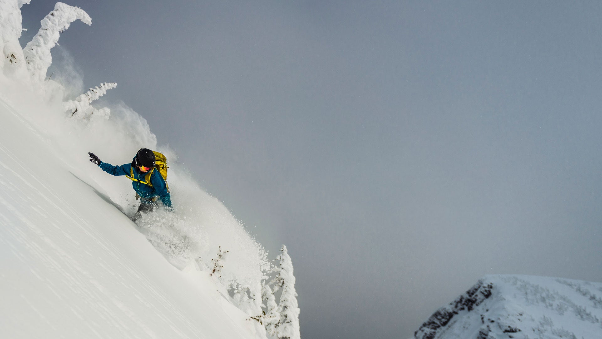 Snowboarder in blue jacket carves through deep powder on steep slope