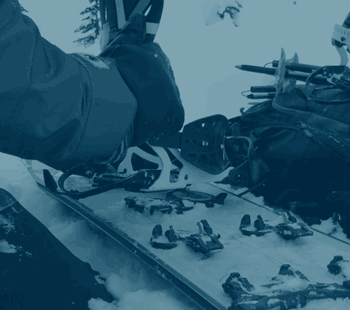 Blue-toned photo of ski touring bindings on snowy splitboard skis