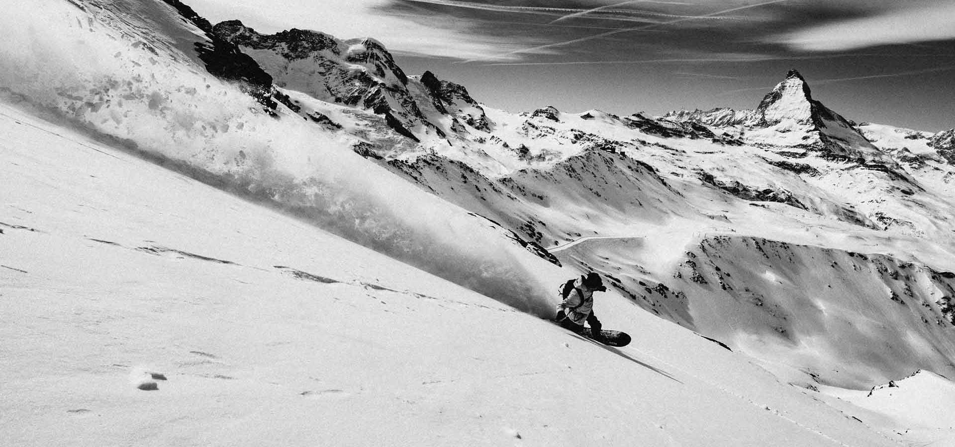 Snowboarder carving deep powder on steep alpine slope, black-and-white