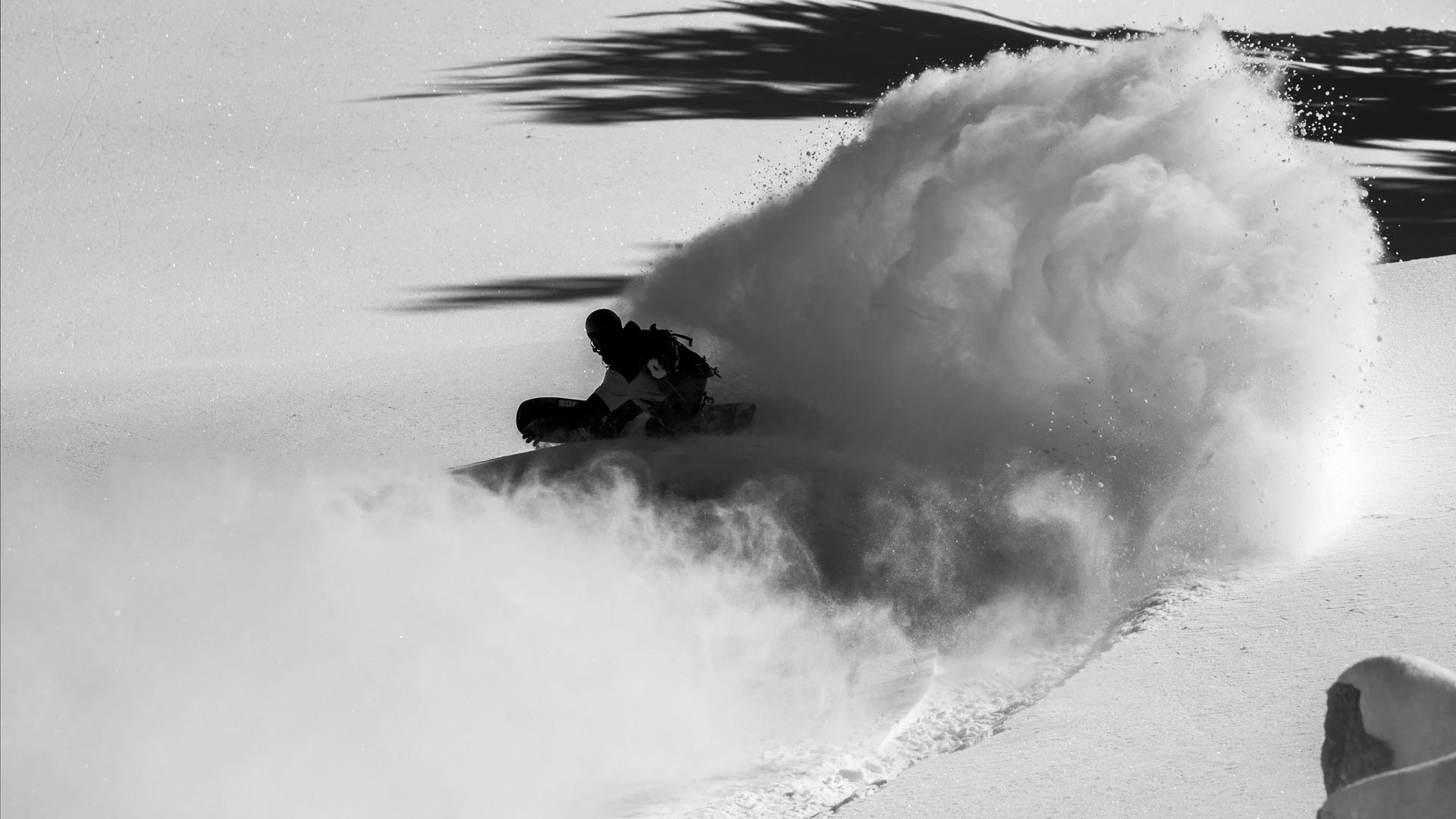 Snowboarder carving deep powder, spraying large snow cloud, black-and-white photo