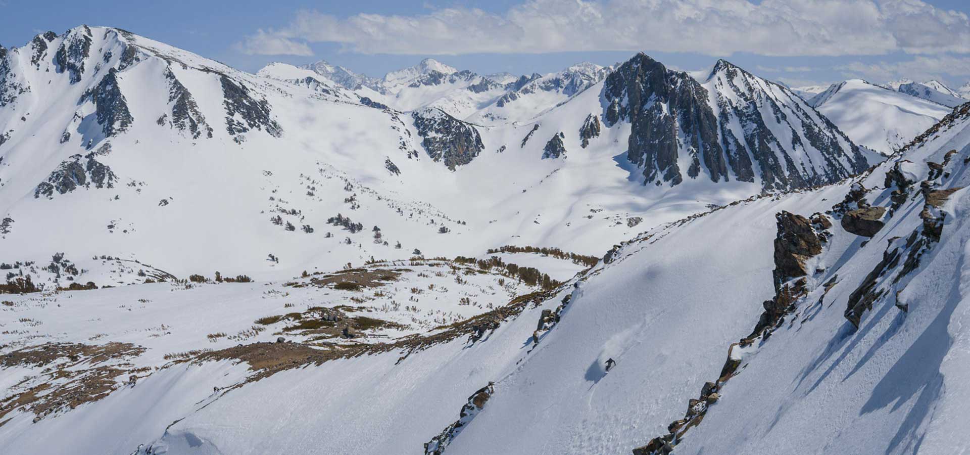 Skier descending steep snowy ridge among jagged rocky mountain peaks