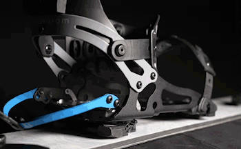 Black snowboard binding with blue strap mounted on board, close-up