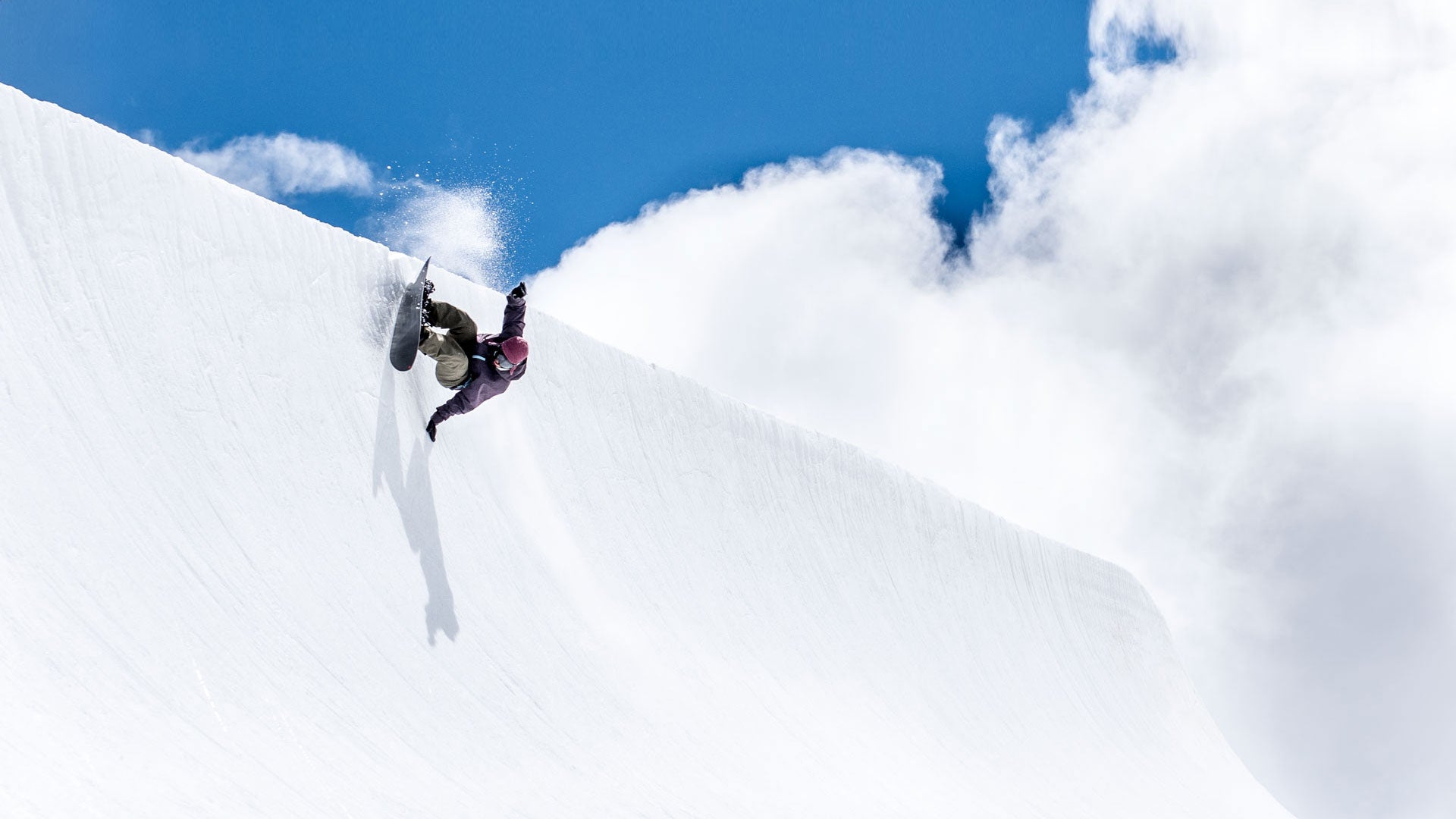 Snowboarder carving up a halfpipe wall against blue sky