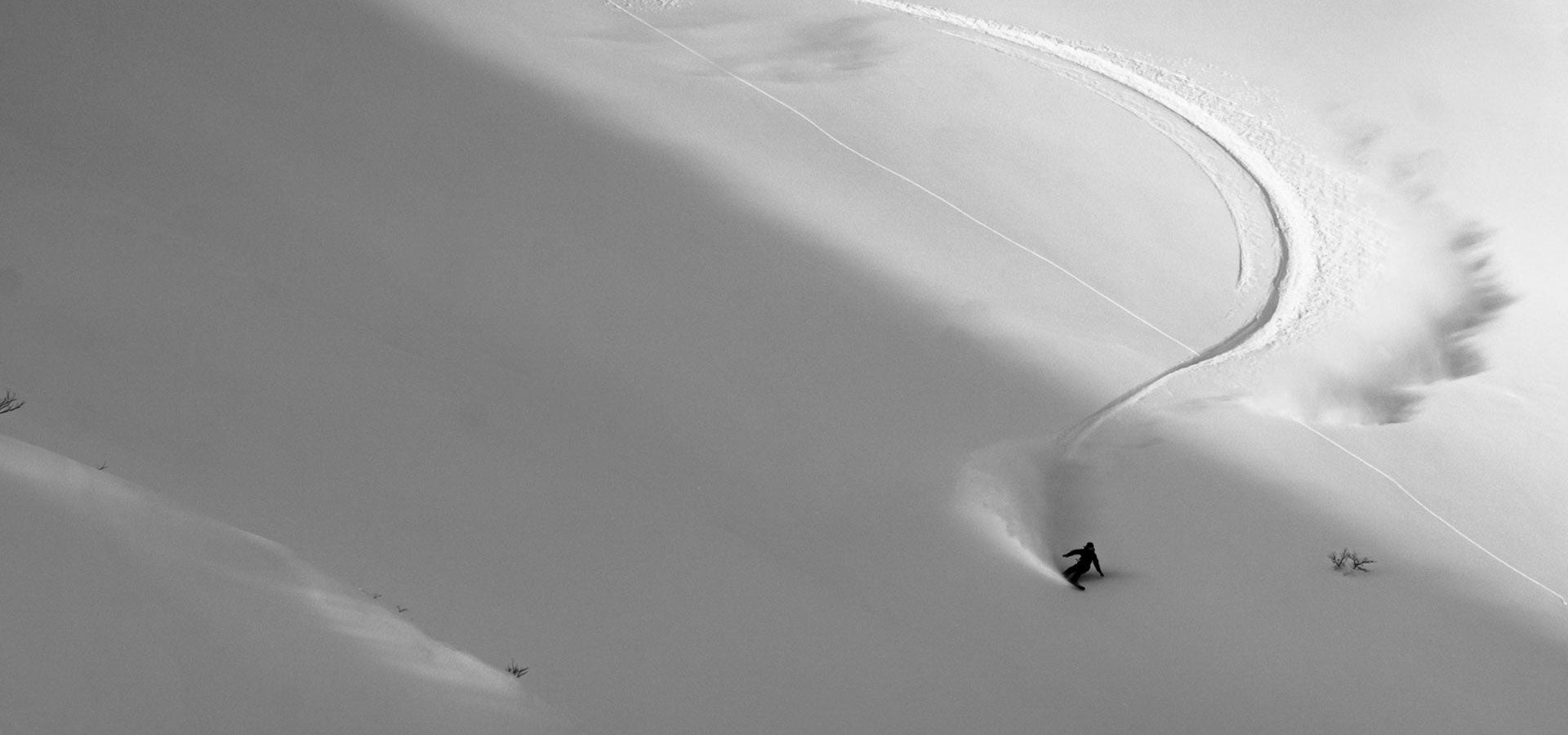 Snowboarder carving curved tracks down steep untouched powder slope