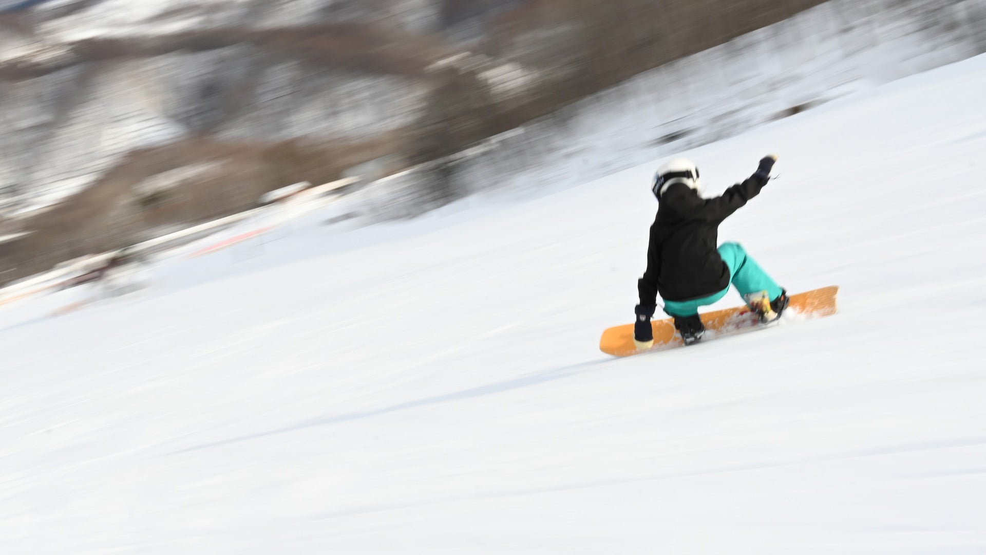 Snowboarder in black jacket carving down snowy slope, orange board