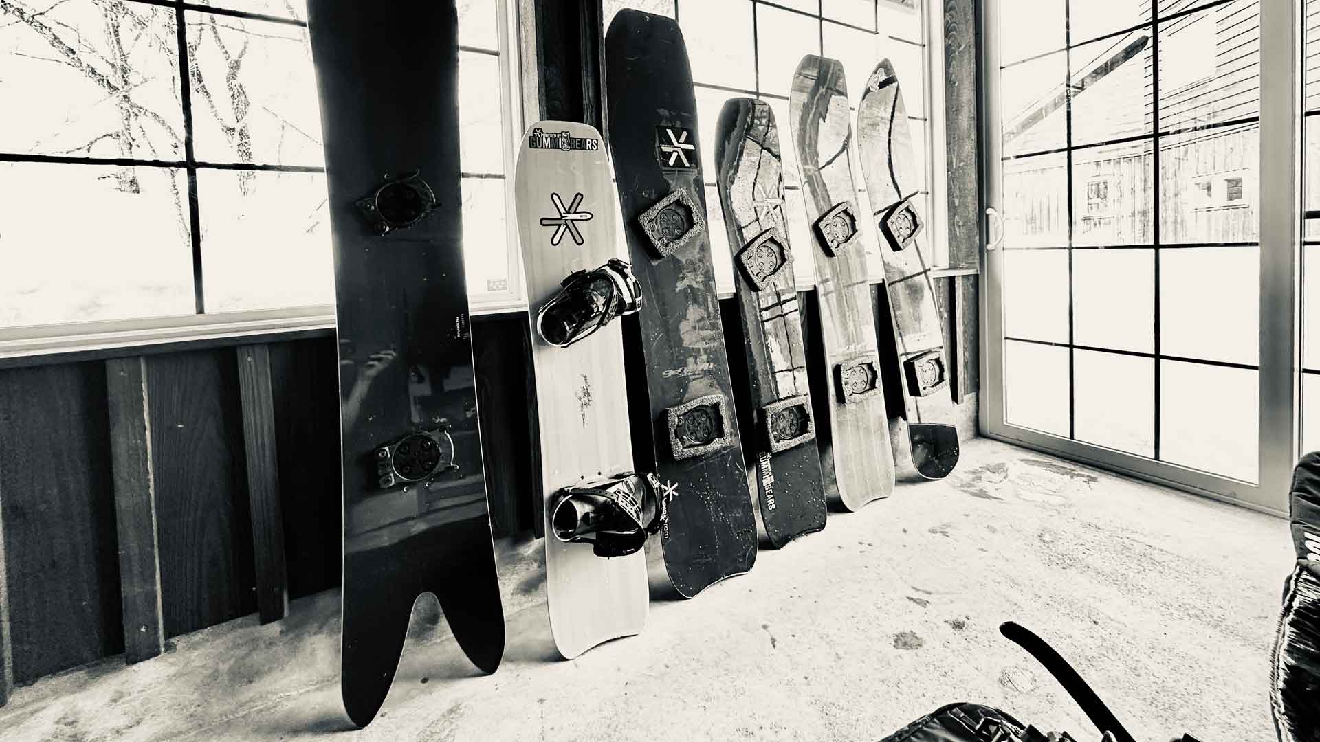 Six snowboards leaning against wall by window, black and white