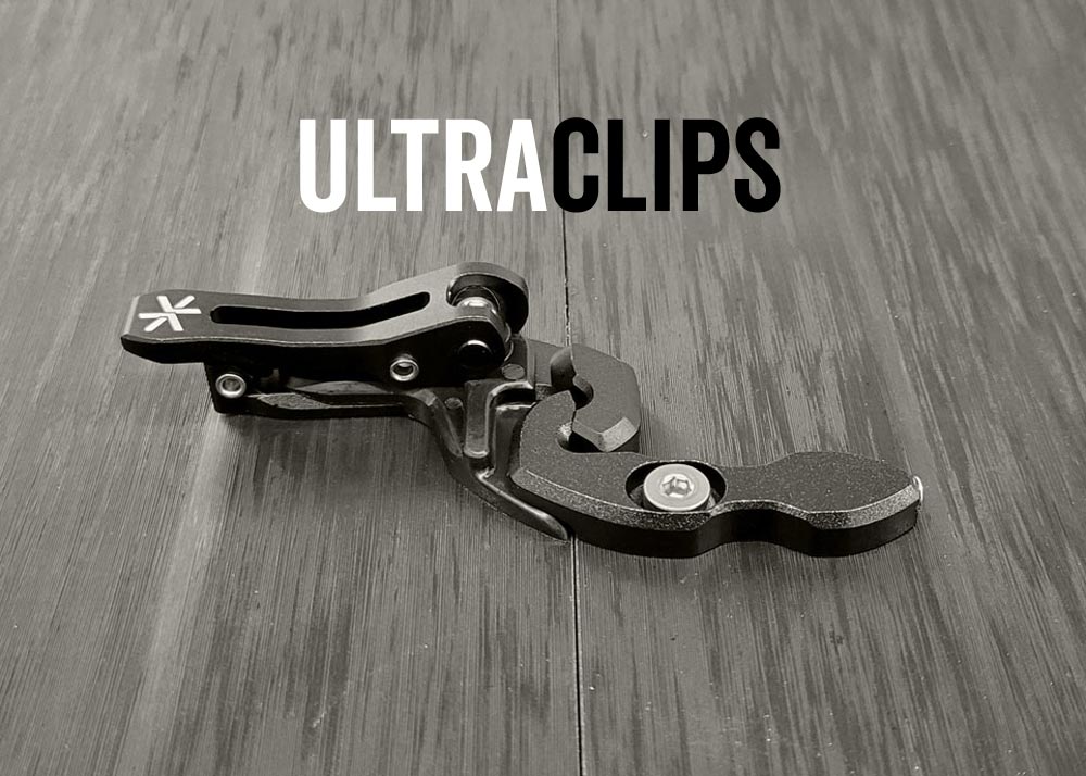 Black metal spring-loaded clip mechanism lying on wood grain surface