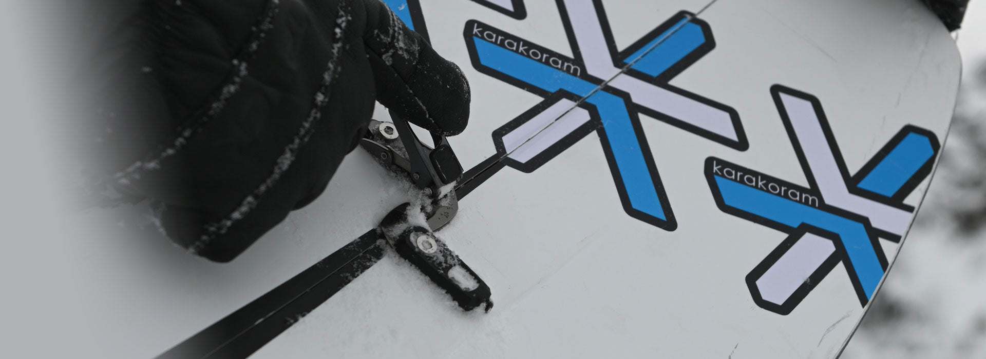 Gloved hand adjusting binding hardware on white splitboard with blue logos