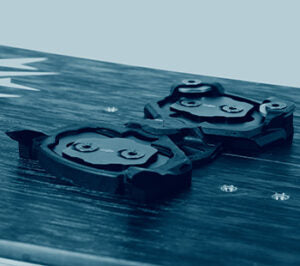Black bike pedal cleats mounted on carbon fiber surface, close-up