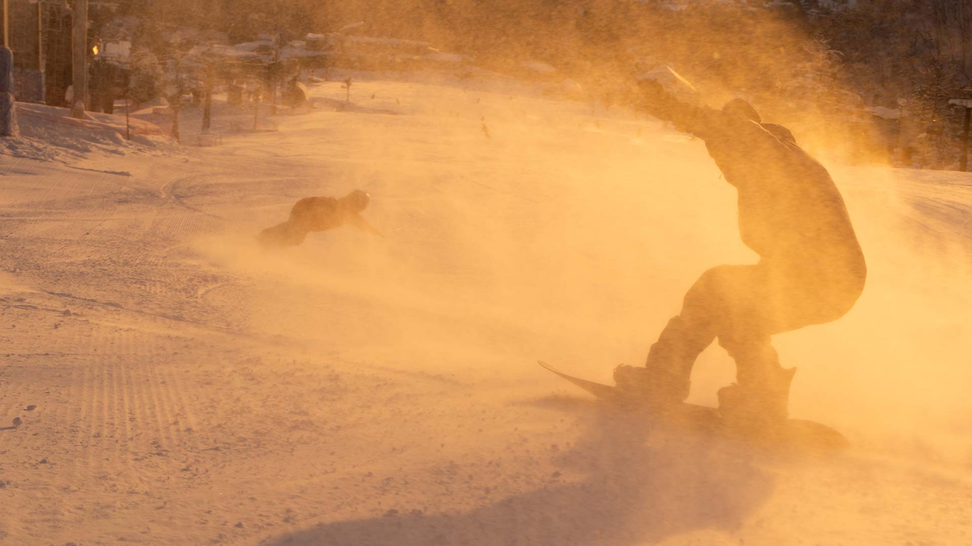 Snowboarder carving through powder spray on slope at golden sunset