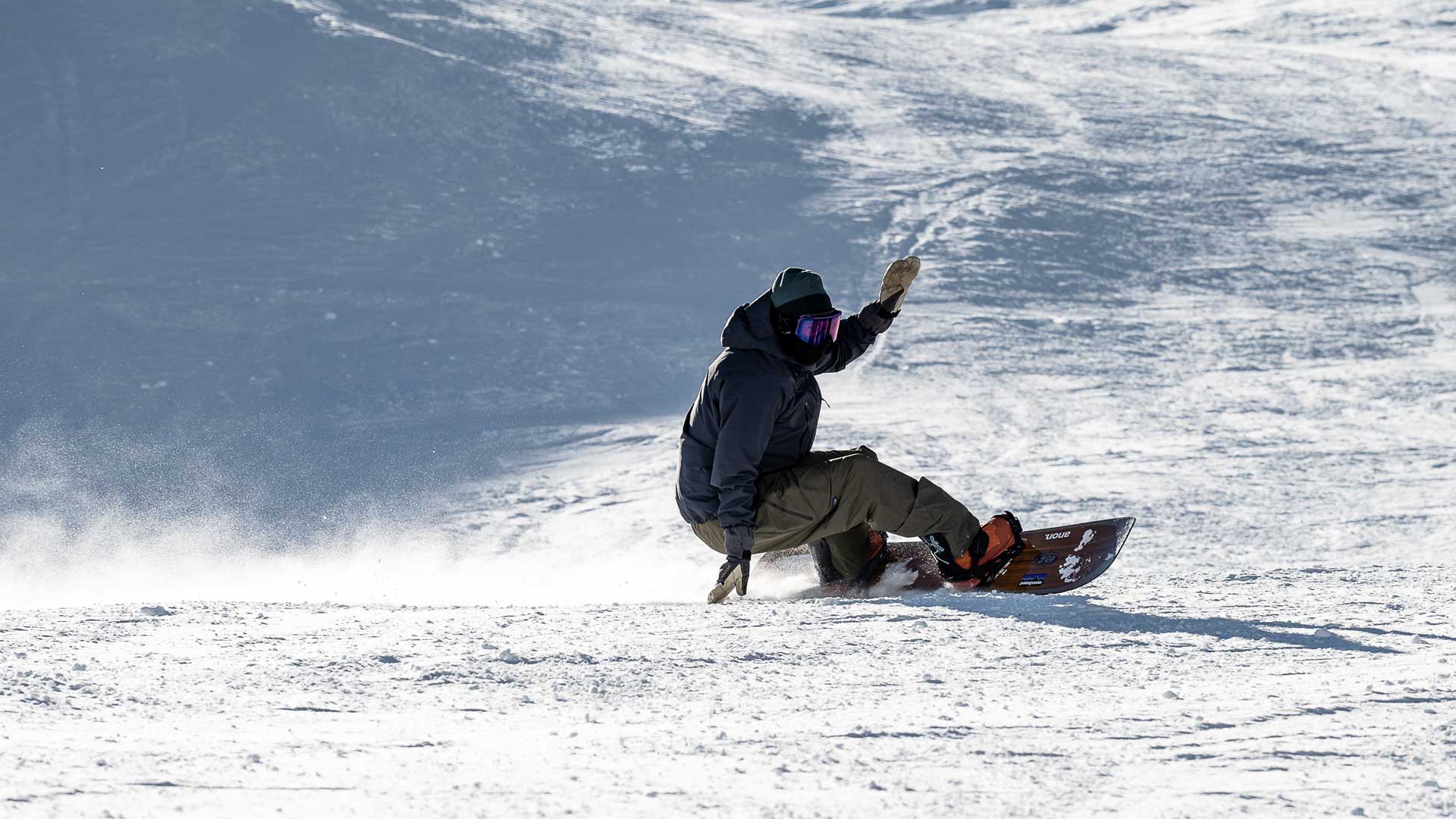 Snowboarder carving turn on snowy slope, hand touching snow