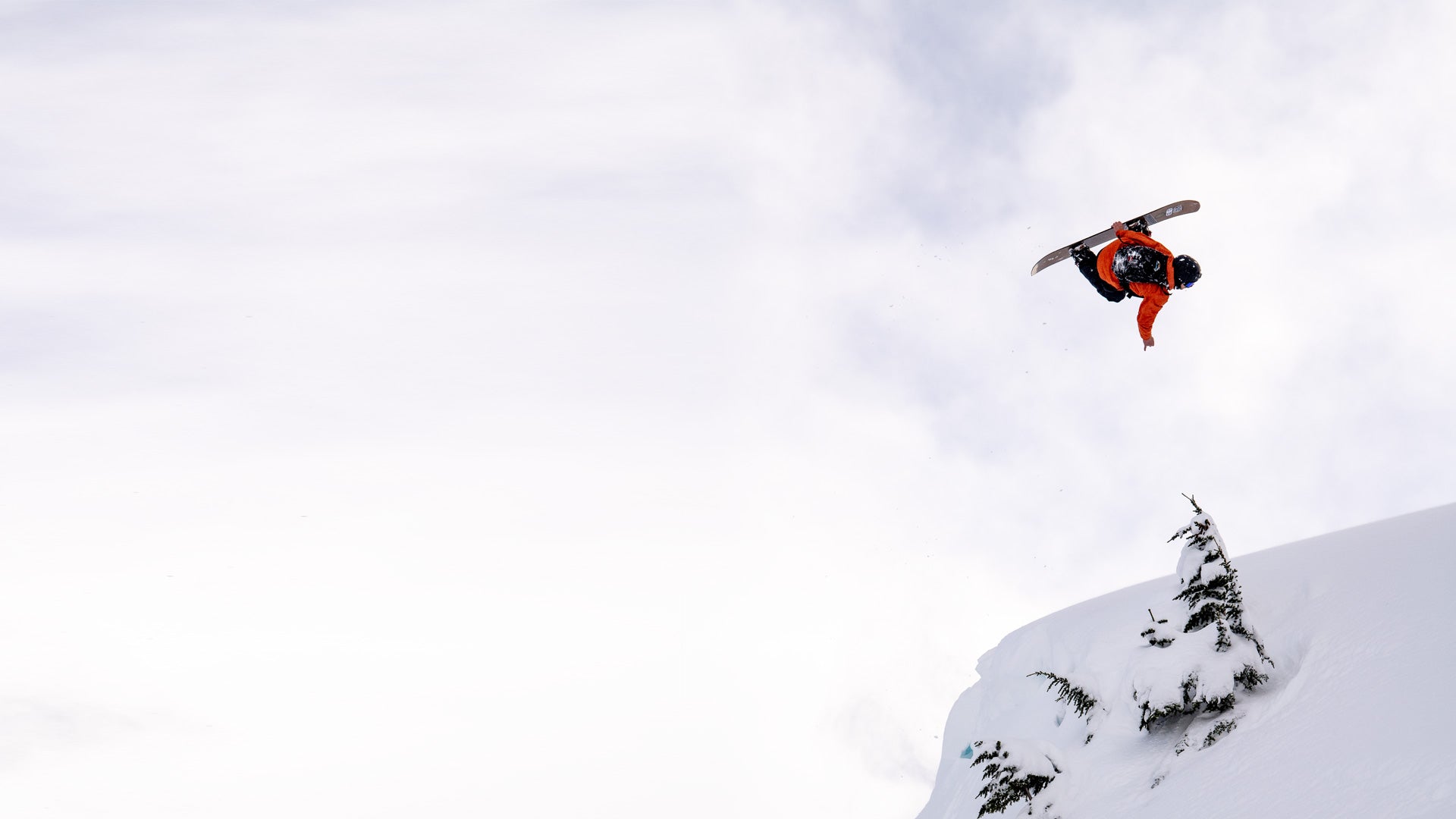Snowboarder in orange jacket grabs board mid-air above snowy ridge